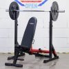 Vitox Fitness Squat rack: A minimalist black and red squat rack featuring two vertical posts with adjustable barbell holders. The frame includes a stabilizing horizontal support bar at the base with adjustable width, allowing for customization to accommodate various barbell exercises like squats and bench presses. The compact design is ideal for home use, with non-slip feet ensuring stability.