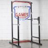 Vitox Fitness - Half power rack VR215: A sturdy black and red weightlifting structure with two vertical posts and adjustable safety bars. It includes a pull-up bar at the top and barbell hooks for squats and bench presses. The frame features multiple height adjustments, with safety arms and a compact design, suitable for home or gym use.